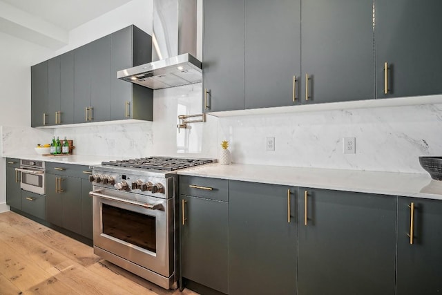 kitchen featuring gray cabinetry, wall chimney exhaust hood, light hardwood / wood-style floors, decorative backsplash, and appliances with stainless steel finishes