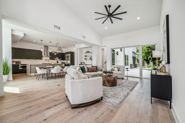 living room with ceiling fan, light wood-type flooring, and high vaulted ceiling