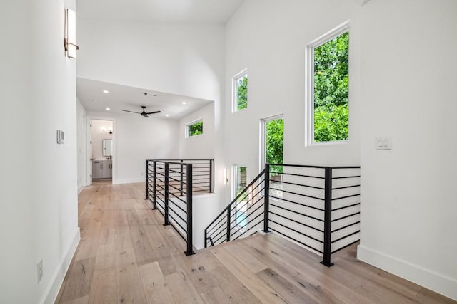 hall featuring light wood-style flooring, recessed lighting, a high ceiling, an upstairs landing, and baseboards