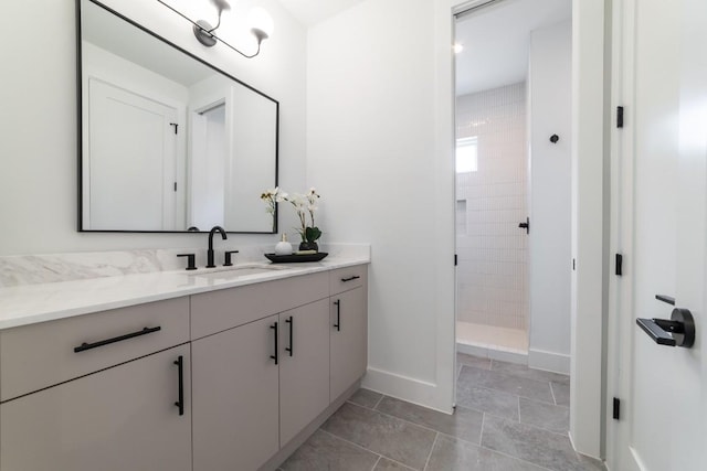 bathroom featuring tile patterned floors, a tile shower, vanity, and baseboards