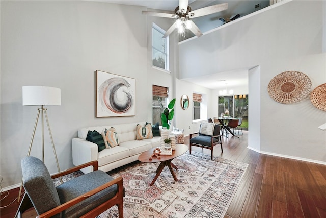 living room with a towering ceiling, ceiling fan with notable chandelier, baseboards, and hardwood / wood-style flooring