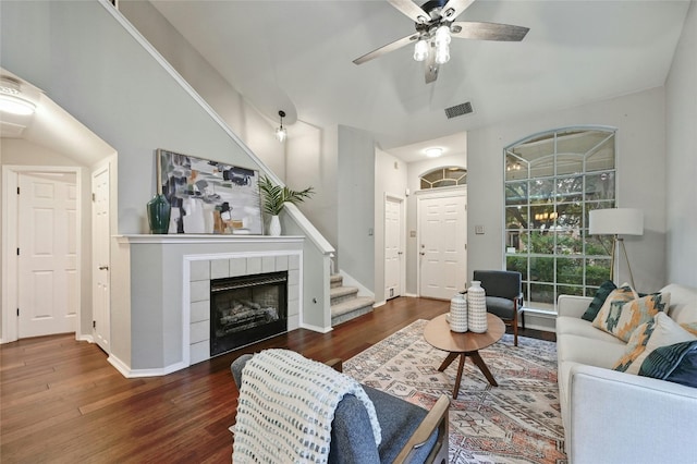 living room featuring stairs, wood finished floors, a tiled fireplace, and ceiling fan