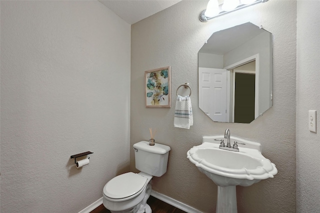 bathroom with baseboards, toilet, wood finished floors, and a textured wall