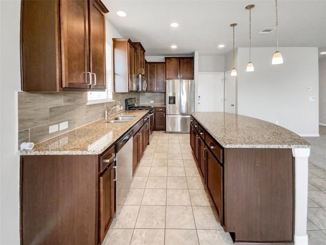 kitchen featuring appliances with stainless steel finishes, sink, hanging light fixtures, a center island, and light stone countertops