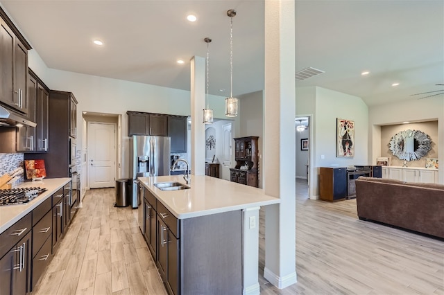 kitchen with light wood-type flooring, stainless steel appliances, a kitchen island with sink, sink, and pendant lighting