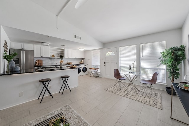 interior space featuring lofted ceiling, stainless steel fridge, a breakfast bar, white cabinetry, and backsplash