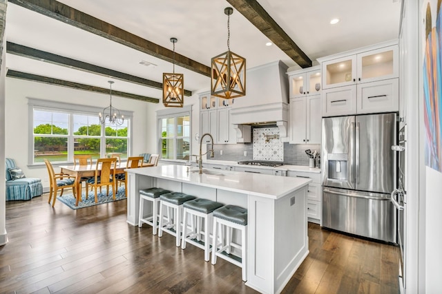 kitchen with a center island with sink, dark hardwood / wood-style flooring, appliances with stainless steel finishes, beamed ceiling, and premium range hood