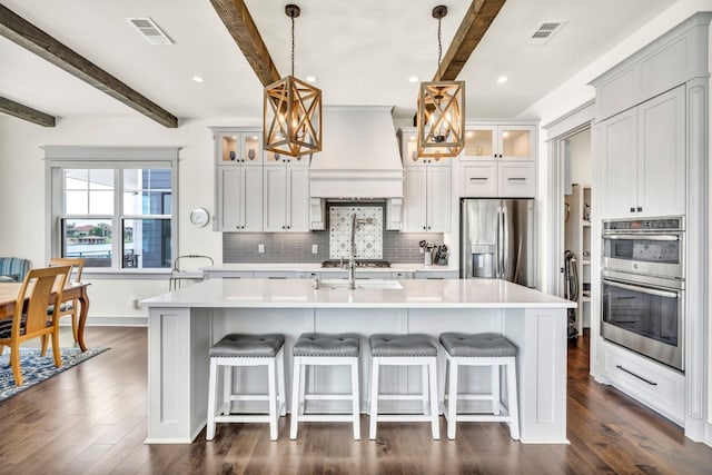 kitchen featuring stainless steel appliances, beamed ceiling, an island with sink, and pendant lighting