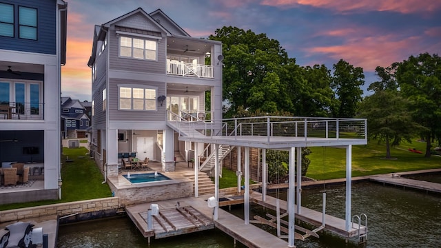 back house at dusk featuring a patio area, a balcony, ceiling fan, and a water view