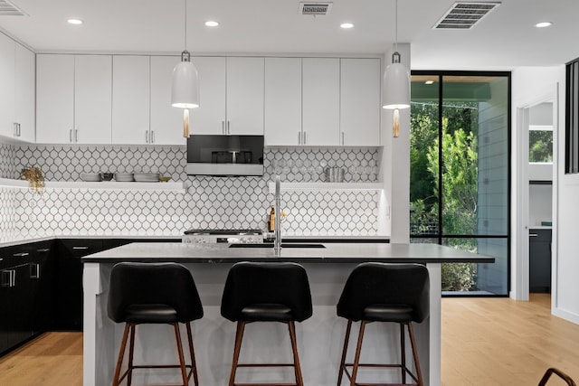 kitchen with hanging light fixtures, light hardwood / wood-style floors, white cabinets, and tasteful backsplash