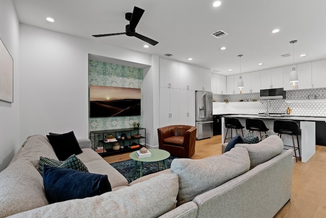 living room with a multi sided fireplace, ceiling fan, light hardwood / wood-style floors, and sink