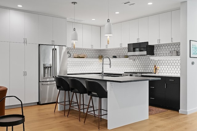 kitchen with light hardwood / wood-style floors, high end fridge, tasteful backsplash, a kitchen island with sink, and sink