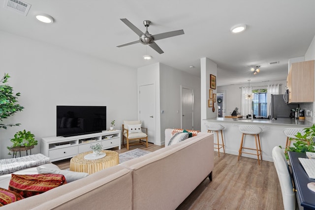 living room featuring ceiling fan with notable chandelier and light hardwood / wood-style floors