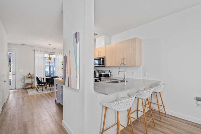 kitchen with light hardwood / wood-style floors, tasteful backsplash, sink, appliances with stainless steel finishes, and light brown cabinetry