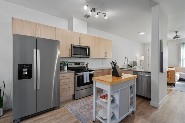 kitchen featuring light wood-type flooring, tasteful backsplash, light brown cabinets, appliances with stainless steel finishes, and ceiling fan