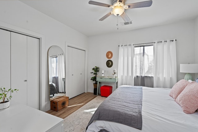 bedroom with ceiling fan, multiple closets, and light hardwood / wood-style floors