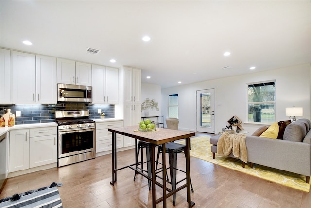 kitchen with light hardwood / wood-style flooring, tasteful backsplash, a kitchen bar, white cabinetry, and appliances with stainless steel finishes