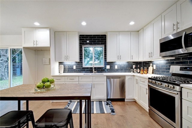 kitchen featuring white cabinets, stainless steel appliances, sink, light hardwood / wood-style flooring, and tasteful backsplash