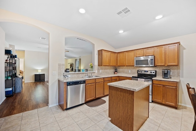 kitchen featuring light tile patterned floors, a center island, stainless steel appliances, and vaulted ceiling