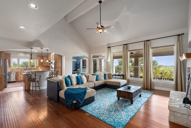 living room featuring a stone fireplace, wood-type flooring, high vaulted ceiling, beamed ceiling, and ceiling fan