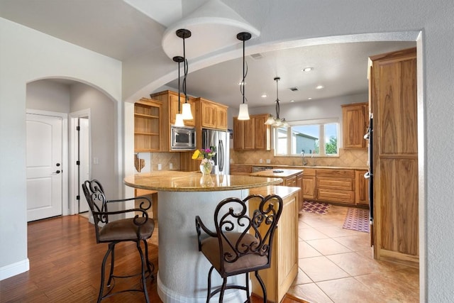 kitchen with a breakfast bar area, light stone counters, tasteful backsplash, hanging light fixtures, and appliances with stainless steel finishes