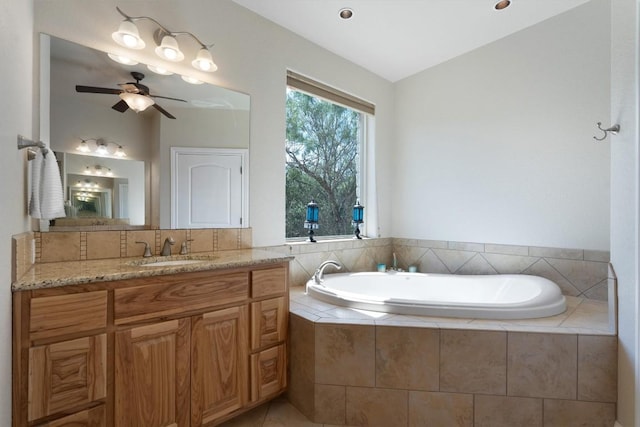 bathroom with a relaxing tiled tub, vanity, vaulted ceiling, and ceiling fan