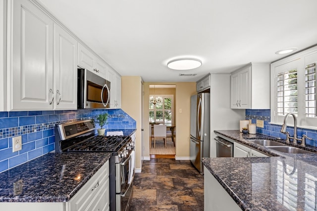 kitchen featuring dark stone counters, sink, decorative backsplash, white cabinetry, and stainless steel appliances