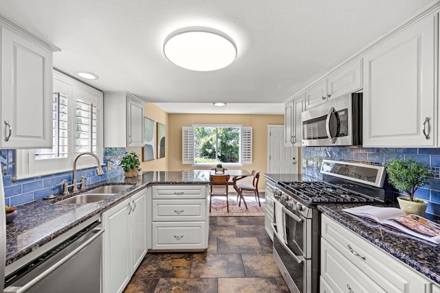 kitchen featuring kitchen peninsula, stainless steel appliances, sink, dark stone countertops, and white cabinets