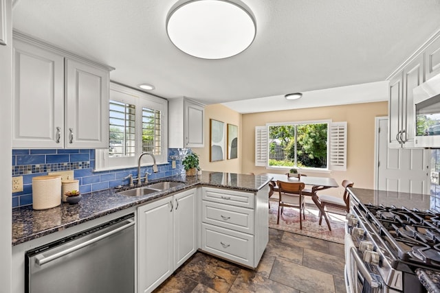 kitchen featuring white cabinetry, sink, stainless steel appliances, kitchen peninsula, and dark stone counters