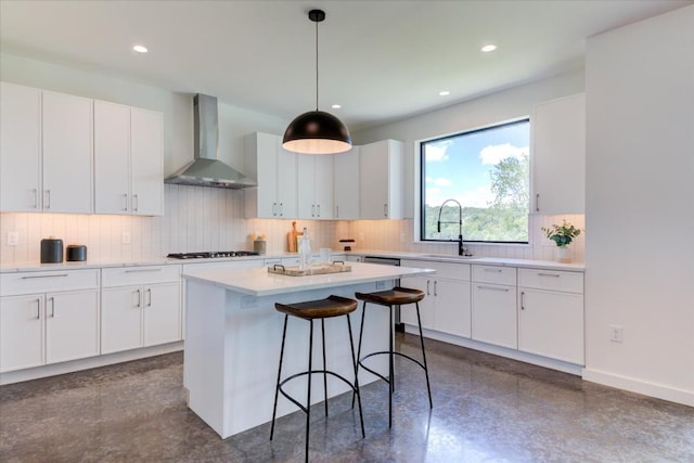 kitchen with sink, white cabinetry, decorative light fixtures, a center island, and wall chimney range hood