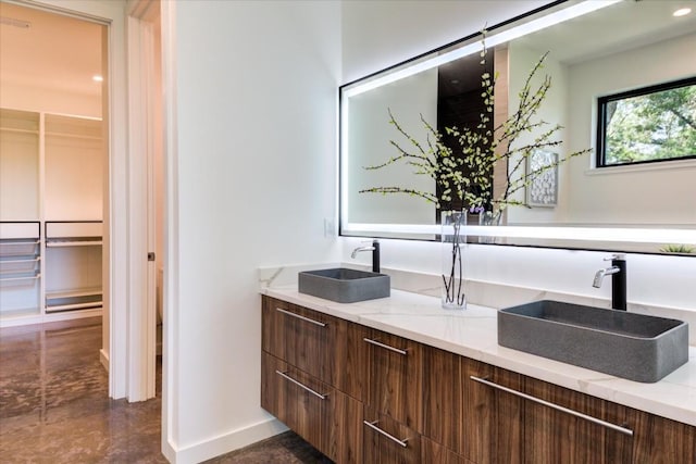 bathroom featuring a spacious closet, double vanity, a sink, and baseboards