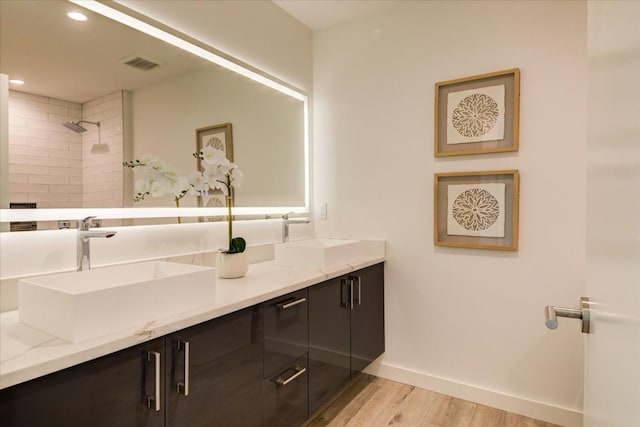 full bath with wood finished floors, tiled shower, a sink, and visible vents