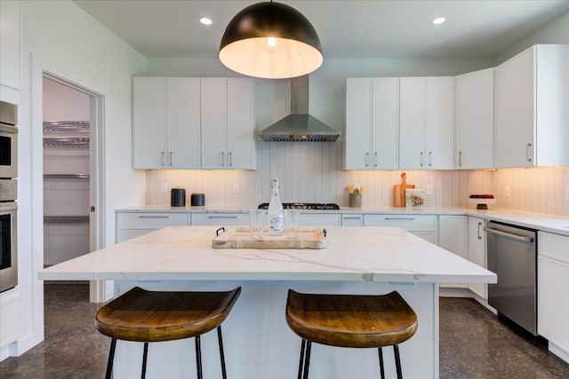 kitchen with wall chimney range hood, a kitchen island, white cabinets, and appliances with stainless steel finishes