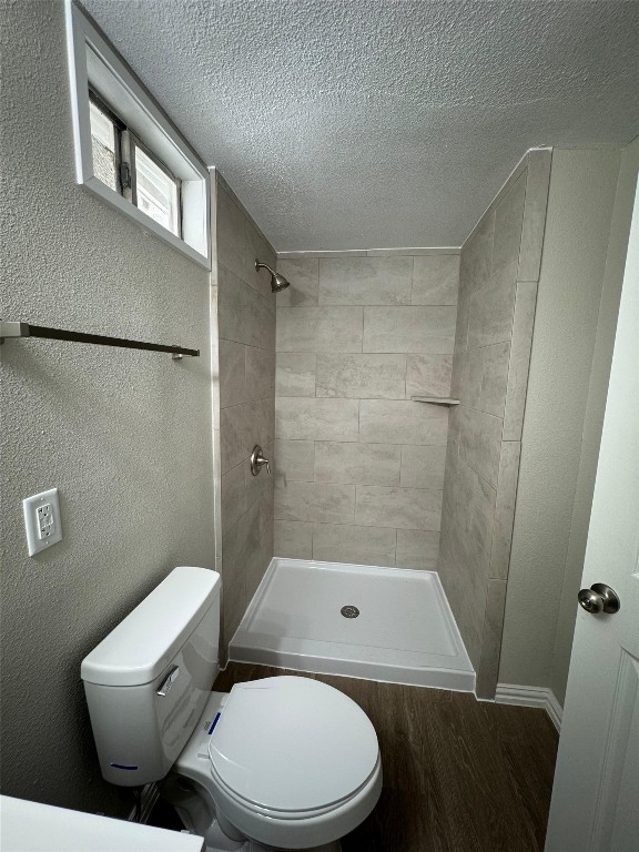 101 S Lockhart St, Manor, TX 78653 - bathroom featuring a textured ceiling, wood finished floors, toilet, and tiled shower