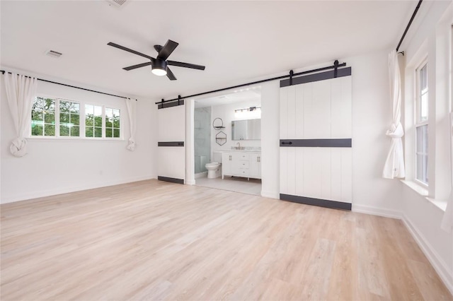 unfurnished bedroom with a barn door, ensuite bathroom, ceiling fan, and light hardwood / wood-style floors