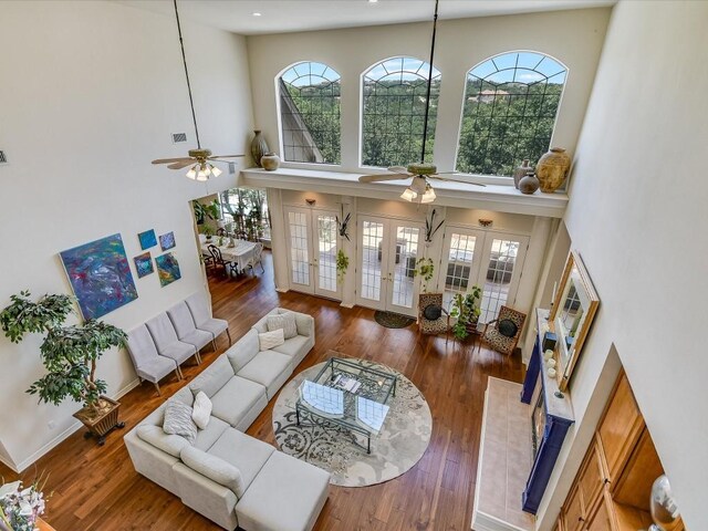 living room with french doors, wood-type flooring, ceiling fan, and a towering ceiling