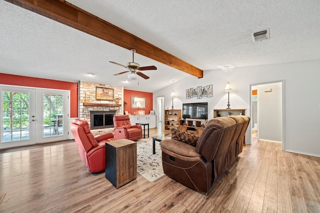 living room with a textured ceiling, vaulted ceiling with beams, a fireplace, ceiling fan, and light hardwood / wood-style flooring