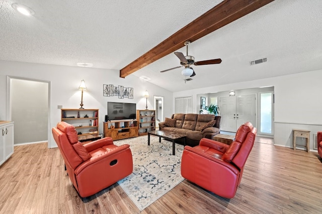 living room featuring ceiling fan, vaulted ceiling with beams, a textured ceiling, and light hardwood / wood-style floors