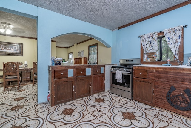 kitchen featuring a textured ceiling, ornamental molding, dark brown cabinetry, stainless steel range, and ceiling fan