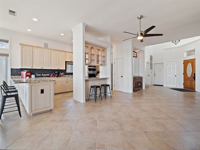 kitchen with a breakfast bar, light stone countertops, ceiling fan, and light tile floors