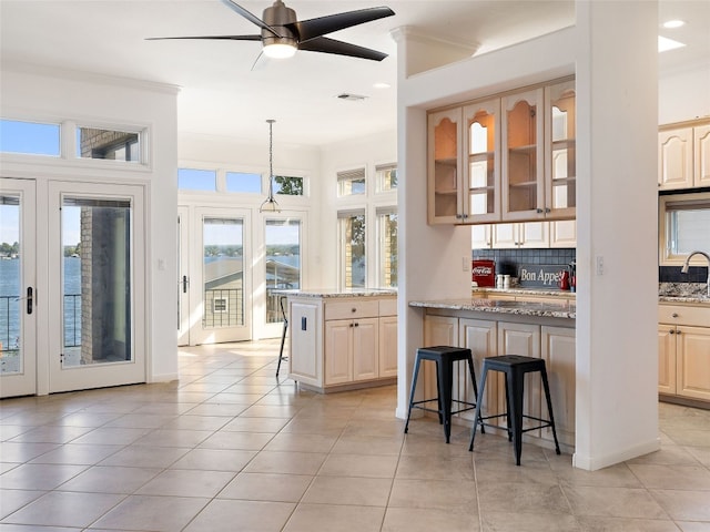 kitchen with tasteful backsplash, crown molding, decorative light fixtures, a kitchen breakfast bar, and light stone countertops