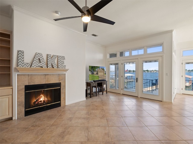 unfurnished living room featuring crown molding, a tile fireplace, a water view, ceiling fan, and light tile floors