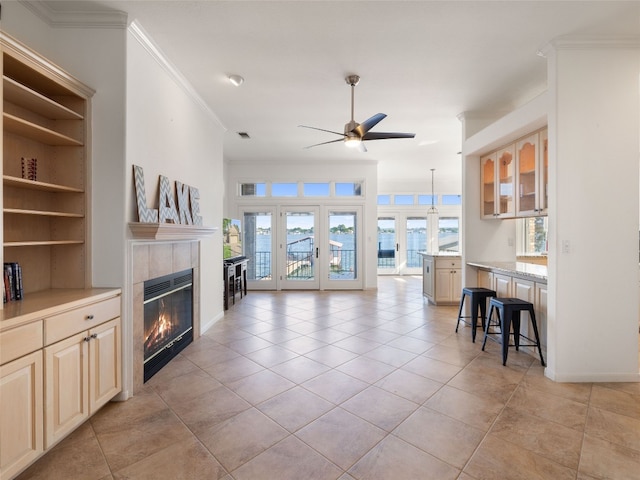 tiled living room featuring crown molding, a wealth of natural light, a tiled fireplace, and ceiling fan