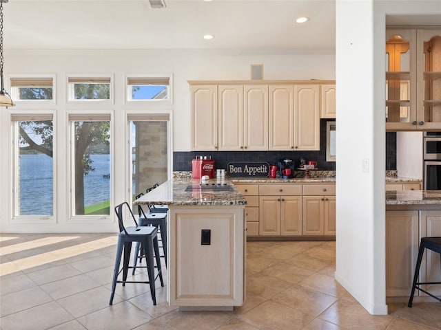 kitchen with decorative light fixtures, dark stone counters, light brown cabinetry, tasteful backsplash, and a kitchen bar