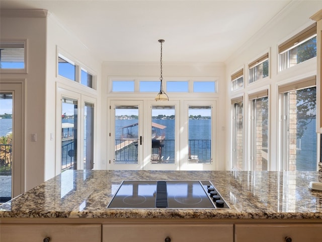 kitchen featuring dark stone countertops, ornamental molding, a water view, black electric cooktop, and pendant lighting