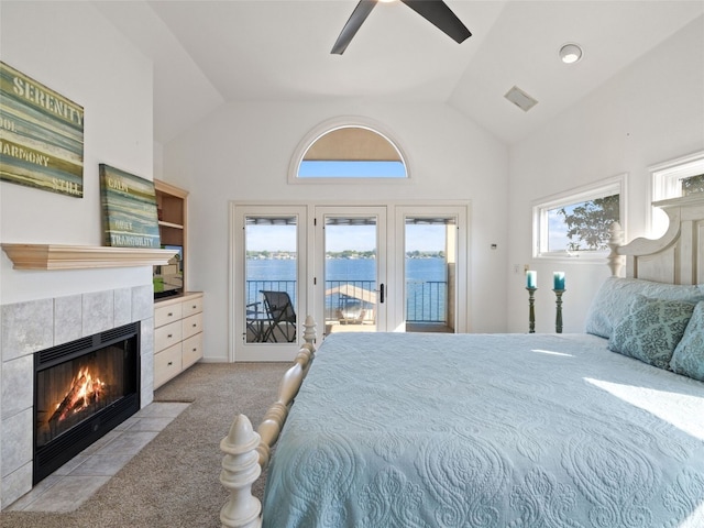 bedroom with access to outside, a tile fireplace, a water view, carpet flooring, and ceiling fan