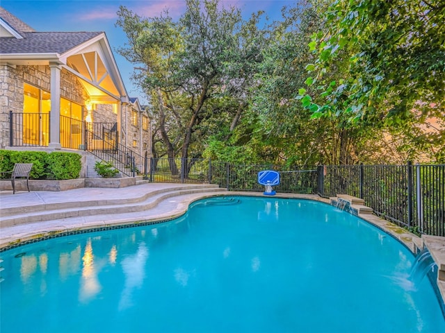 pool at dusk featuring pool water feature and a patio area