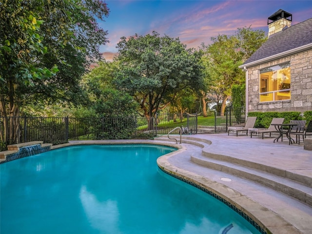 pool at dusk with pool water feature and a patio area