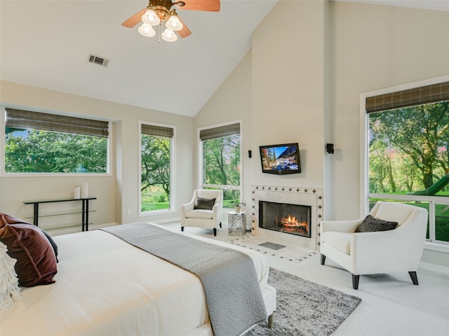 carpeted bedroom featuring a tiled fireplace, ceiling fan, and high vaulted ceiling