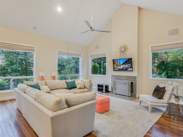 living room with ceiling fan, dark hardwood / wood-style floors, high vaulted ceiling, and a tiled fireplace